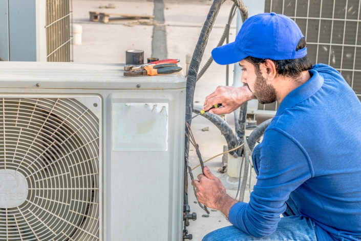 a professional electrician man is fixing a heavy duty unit of ce AC system maintenance